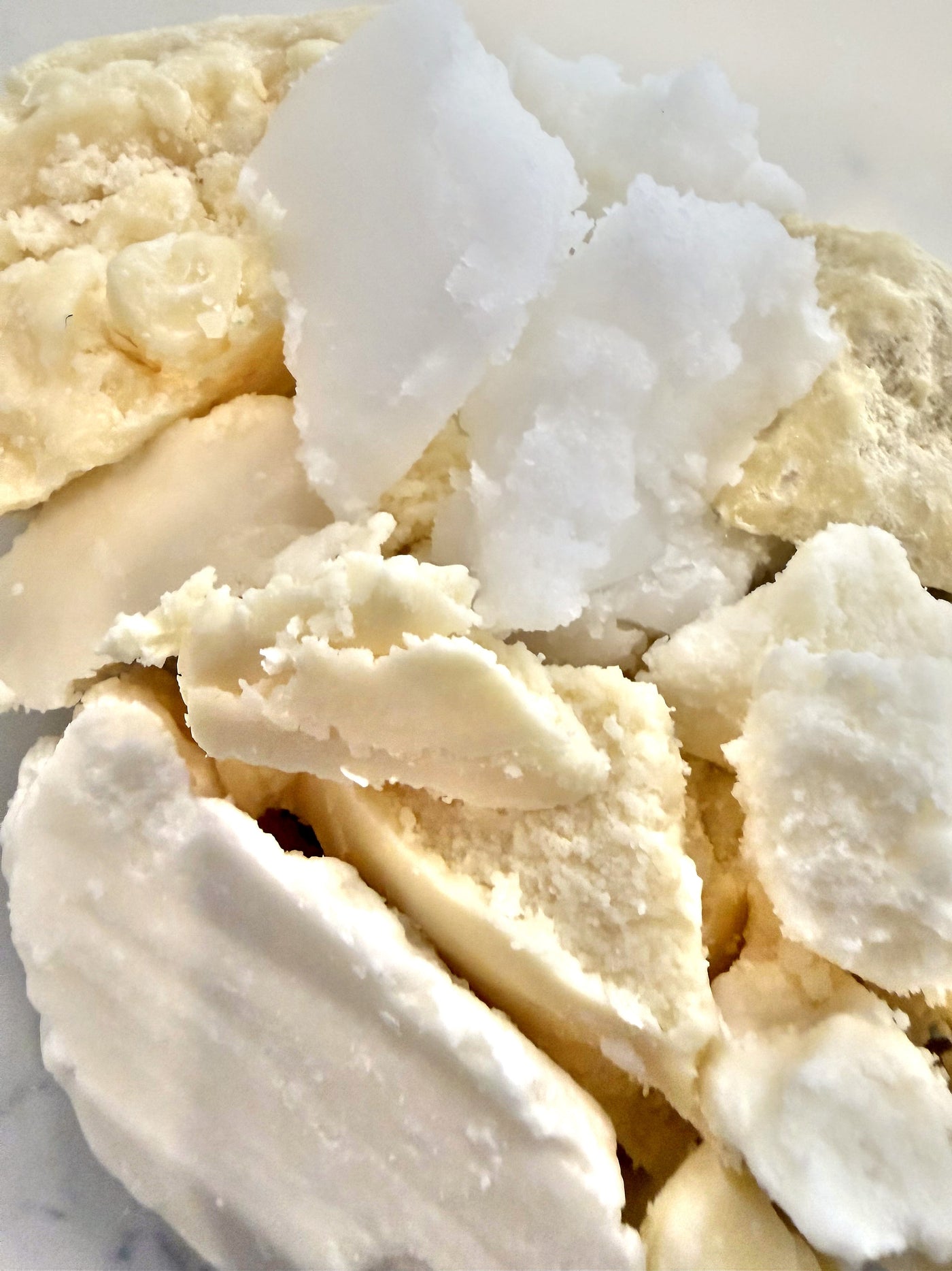 Raw botanical butters in cream and ivory shades, broken into chunks on a marble surface