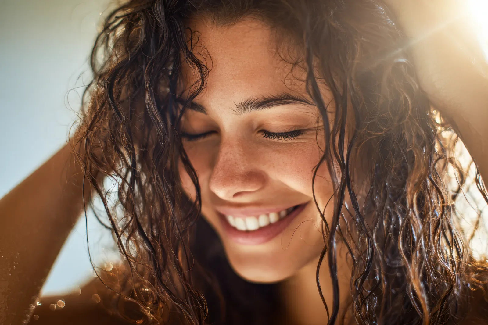 Smiling woman washing her wet curly hair in warm sunlight