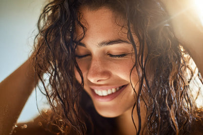 Smiling woman washing her wet curly hair in warm sunlight