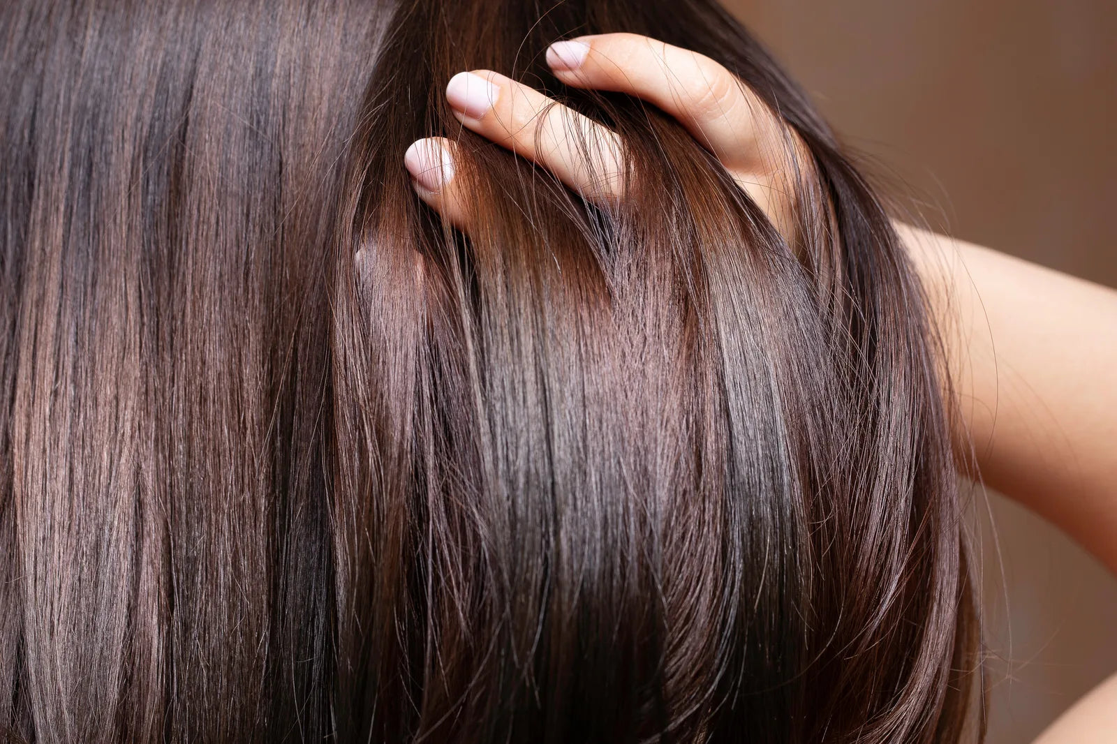 Hand gliding through sleek, glossy brown hair after using Murumuru Rich Reconstruction Hair Mask